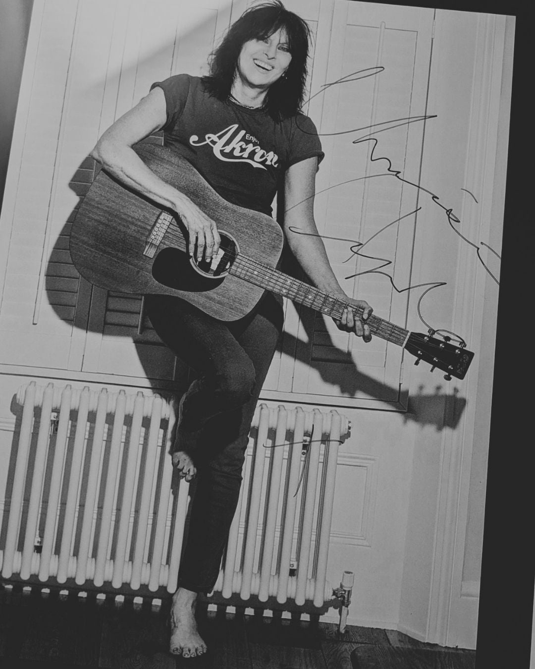 Chrissie Hynde smiling and holding an acoustic guitar, wearing an Akron t-shirt, in a black and white photograph personally signed by Hynde